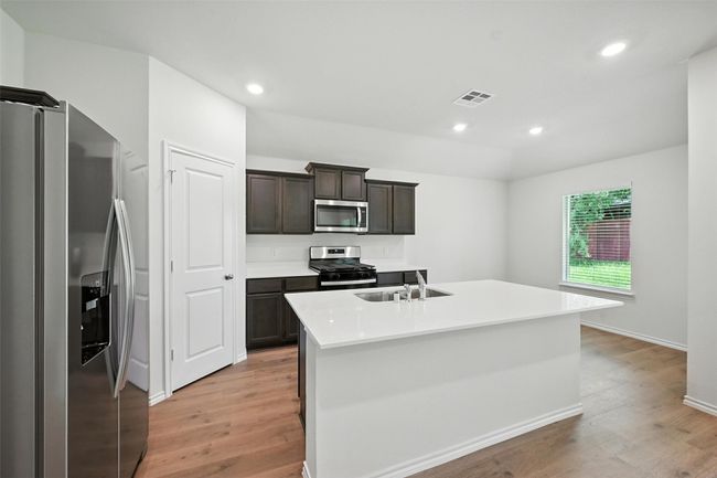 Kitchen with stainless steel appliances, light wood-style flooring, a kitchen island with sink, recessed lighting, and light countertops | Image 6