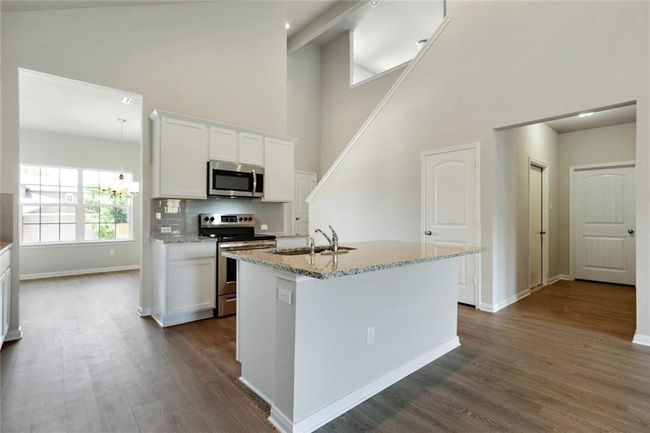 Kitchen with stainless steel appliances, a sink, high vaulted ceiling, light stone countertops, and white cabinets | Image 7