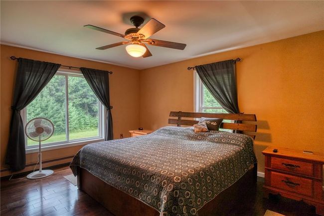 Bedroom featuring ceiling fan, multiple windows, dark hardwood / wood-style floors, and a baseboard heating unit | Image 22