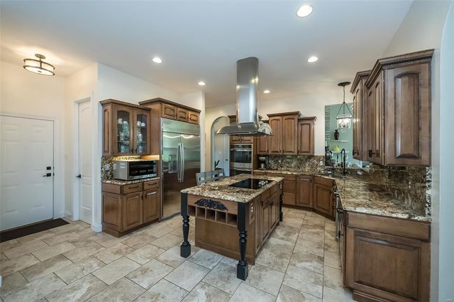 Kitchen featuring stainless steel appliances, dark stone countertops, island range hood, and tasteful backsplash | Image 17