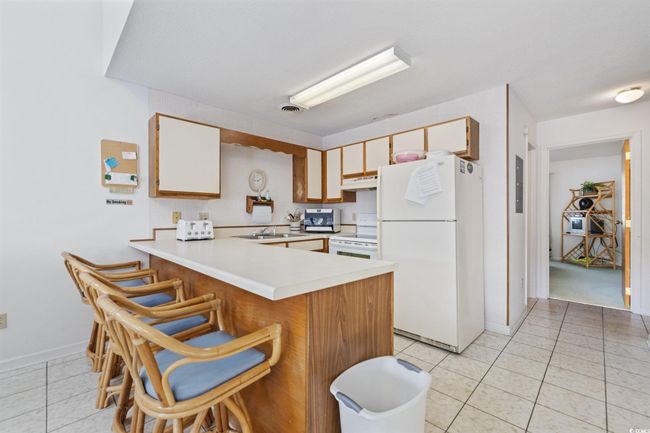 Kitchen with white appliances, a peninsula, light countertops, and light tile patterned floors | Image 7