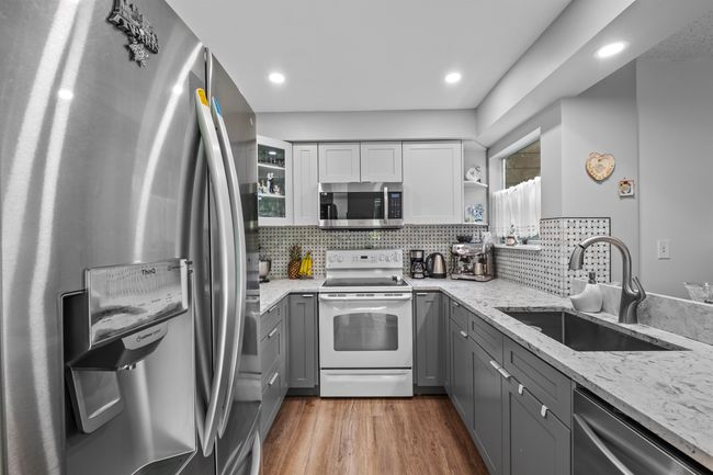 Kitchen with stainless steel appliances, gray cabinets, light stone counters, tasteful backsplash, and recessed lighting | Image 4