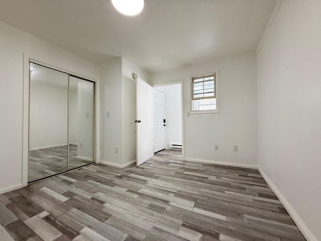 bedroom featuring wood finished floors, a baseboard heating unit, baseboards, and a closet | Image 11