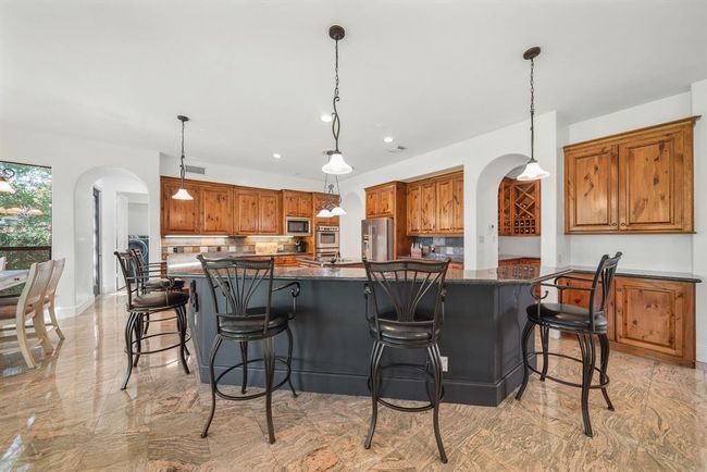 Surrounded by custom cabinets with under mount lighting, granite counters and tiled back splashes, the kitchen has a high ceiling with recessed lighting, pre-wiring for ceiling speakers, a built-in desk & tile flooring. The arched opening on the left leads to a full bath and the utility room. | Image 13
