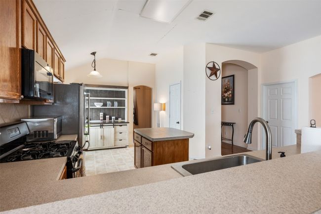 Kitchen with stainless steel gas range oven, visible vents, a sink, arched walkways, and black microwave | Image 15