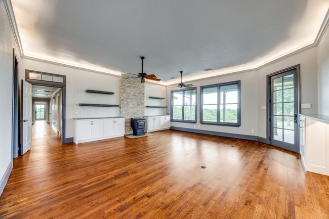 Unfurnished living room featuring a wood stove, a ceiling fan, ornamental molding, wood finished floors, and healthy amount of natural light | Image 8