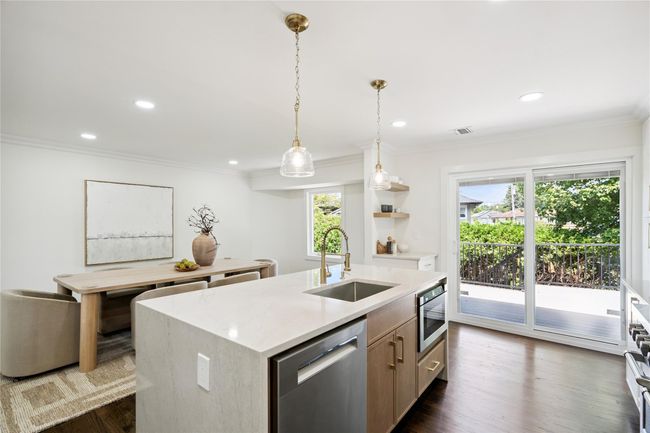 Kitchen featuring stainless steel appliances, a kitchen island with sink, light countertops, dark wood finished floors, and crown molding | Image 8