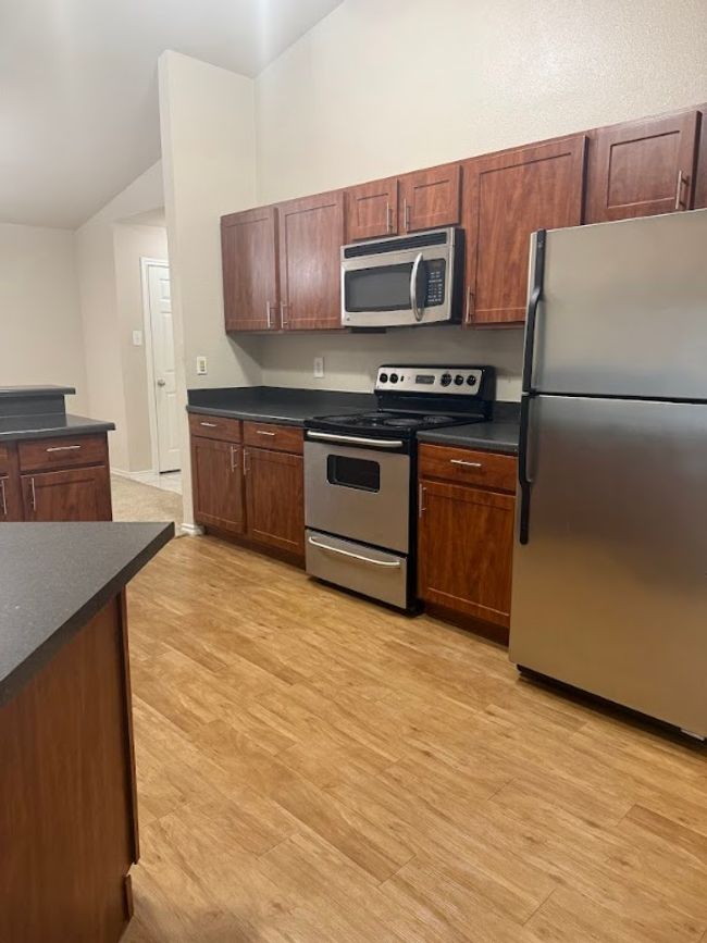 Kitchen with appliances with stainless steel finishes, dark countertops, lofted ceiling, and light wood-type flooring | Image 6