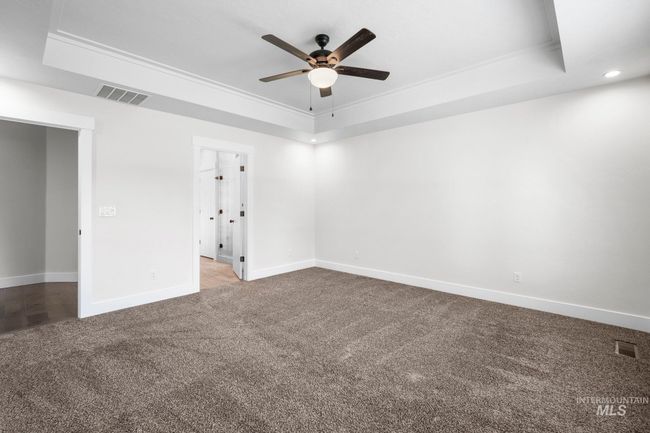 Carpeted empty room with a raised ceiling, a ceiling fan, ornamental molding, and recessed lighting | Image 24
