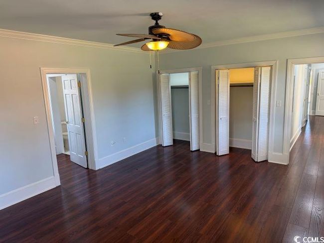 Unfurnished bedroom with multiple closets, dark wood-type flooring, ceiling fan, and crown molding | Image 15