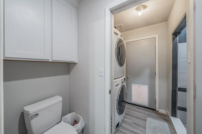 Washroom with a textured ceiling, light hardwood / wood-style flooring, and stacked washer / dryer | Image 4