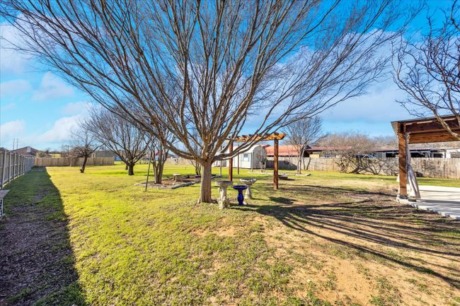 Beautiful backyard with mature trees, lush grass, and a flowerbed, featuring a covered patio with dedicated dining space for outdoor enjoyment. | Image 26