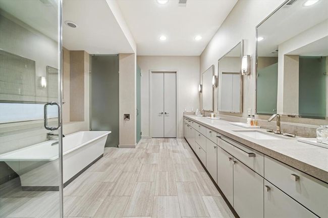 Sophisticated simplicity at its best - the PRIMARY BATH (15 X 12) features walk-in frameless glass front shower (subway tile surround/dual shower heads/stone flooring), Kohler soaking tub (wall mounted faucet, stone tile flooring, stone counters/backsplash, 2 sinks with designer fixtures, soft close doors/cabinets, 3 metal-framed mirrors and four wall-mounted light sconces, papered walls, recessed lighting, linen closet, frosted glass private water closet. | Image 23