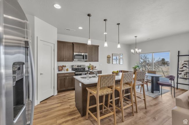 Kitchen featuring an inviting chandelier, hanging light fixtures, an island with sink, appliances with stainless steel finishes, and dark brown cabinetry | Image 9