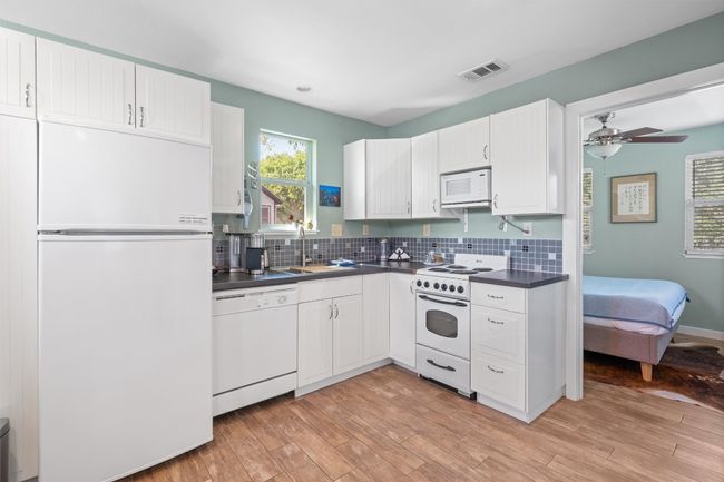 Kitchen featuring white appliances, decorative backsplash, a sink, dark countertops, and visible vents | Image 30