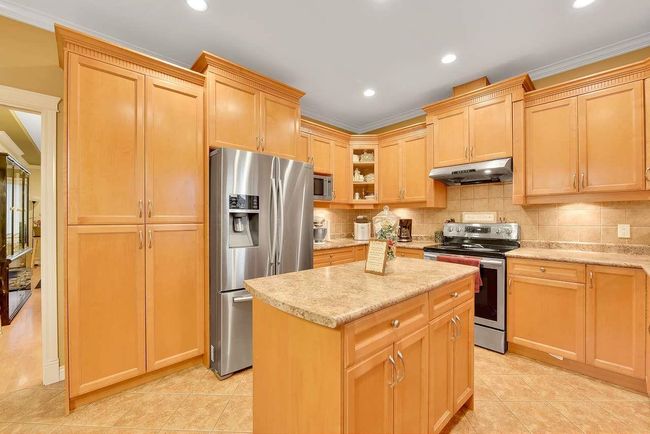 Kitchen with appliances with stainless steel finishes, under cabinet range hood, a kitchen island, decorative backsplash, and light tile patterned flooring | Image 25