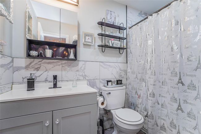 Bathroom with curtained shower, vanity, toilet, and tile walls | Image 15