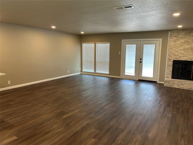 Unfurnished living room with dark wood finished floors, baseboards, recessed lighting, french doors, and a fireplace | Image 19
