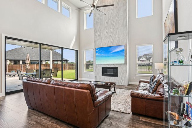 Living area featuring a high ceiling, ceiling fan, dark wood-style floors, and a high end fireplace | Image 8