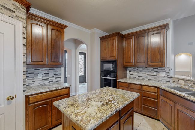 Kitchen with arched walkways, a sink, backsplash, light stone countertops, and black appliances | Image 10