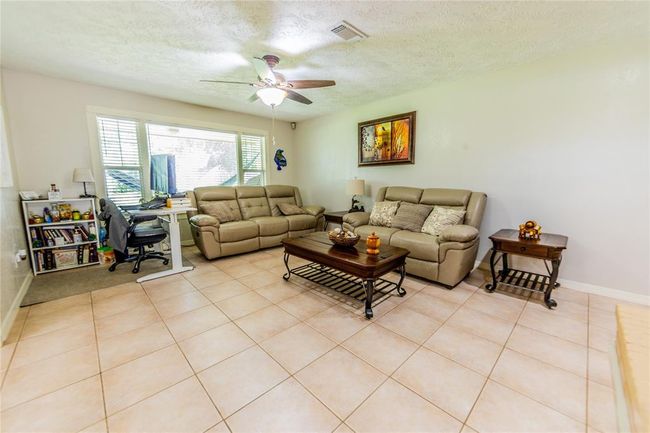 Bright and spacious living room with tile flooring, a ceiling fan, and large windows for plenty of natural light. | Image 10
