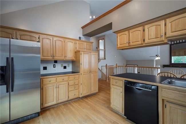 Kitchen with stainless steel fridge with ice dispenser, black dishwasher, light wood finished floors, ceiling fan, and a sink | Image 15