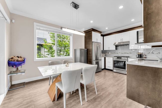 Kitchen featuring stainless steel appliances, under cabinet range hood, ornamental molding, decorative backsplash, and white cabinets | Image 5