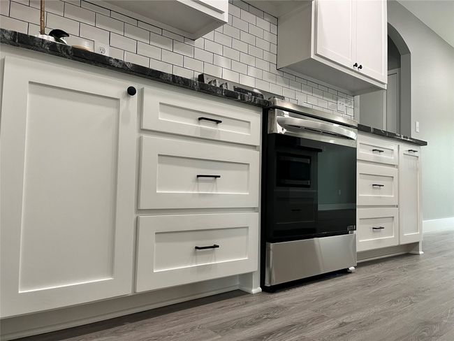 Kitchen featuring light wood finished floors, decorative backsplash, and white cabinets | Image 7
