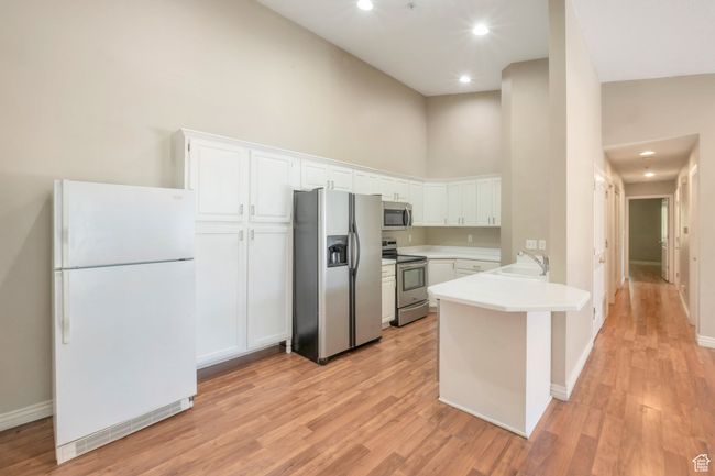Kitchen featuring appliances with stainless steel finishes, a towering ceiling, a peninsula, white cabinets, and light wood finished floors | Image 4