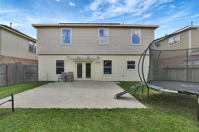 This photo shows the back of a two-story house with beige siding. It features a spacious concrete patio, and a grassy yard. The area is fenced, offering privacy and a great space for outdoor activities. | Image 44