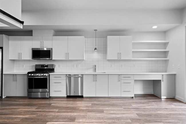 Kitchen with stainless steel appliances, a sink, light countertops, decorative backsplash, and open shelves | Image 10