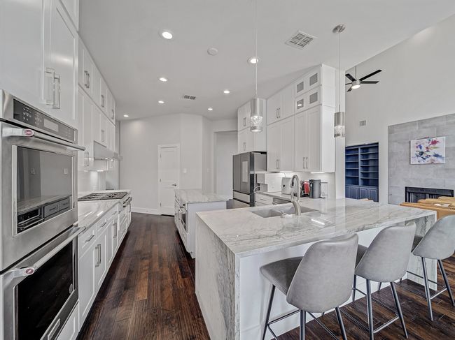 Kitchen featuring appliances with stainless steel finishes, a kitchen island, dark wood finished floors, light stone countertops, and a sink | Image 8