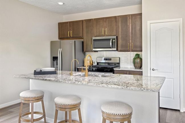 This spacious kitchen features high ceilings, Woodmont Dakota cabinets in Smolder stain, Granite countertops in Diamond Antico, Whirlpool stainless steel appliances, modern tile backsplash, recessed lighting, huge kitchen island with sink and gorgeous Moen kitchen faucet in Brushed Gold, added space for breakfast bar, and a pantry all overlooking your huge family room. | Image 5