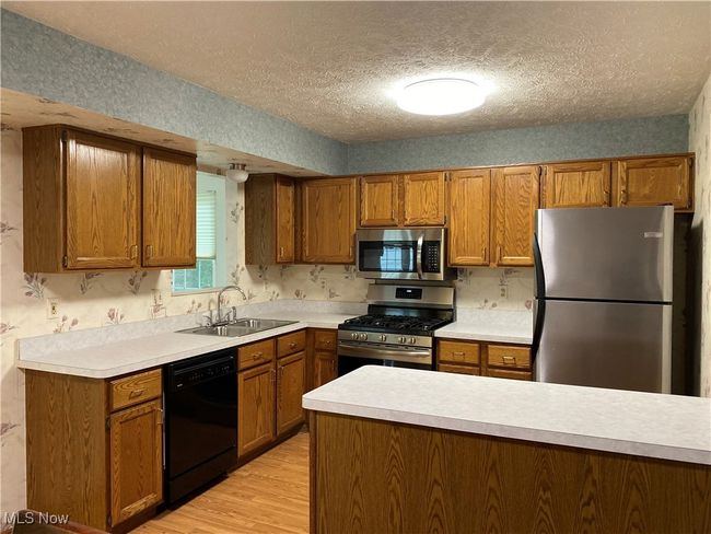 Kitchen featuring stainless steel appliances, a sink, brown cabinetry, a textured ceiling, and light wood-type flooring | Image 28