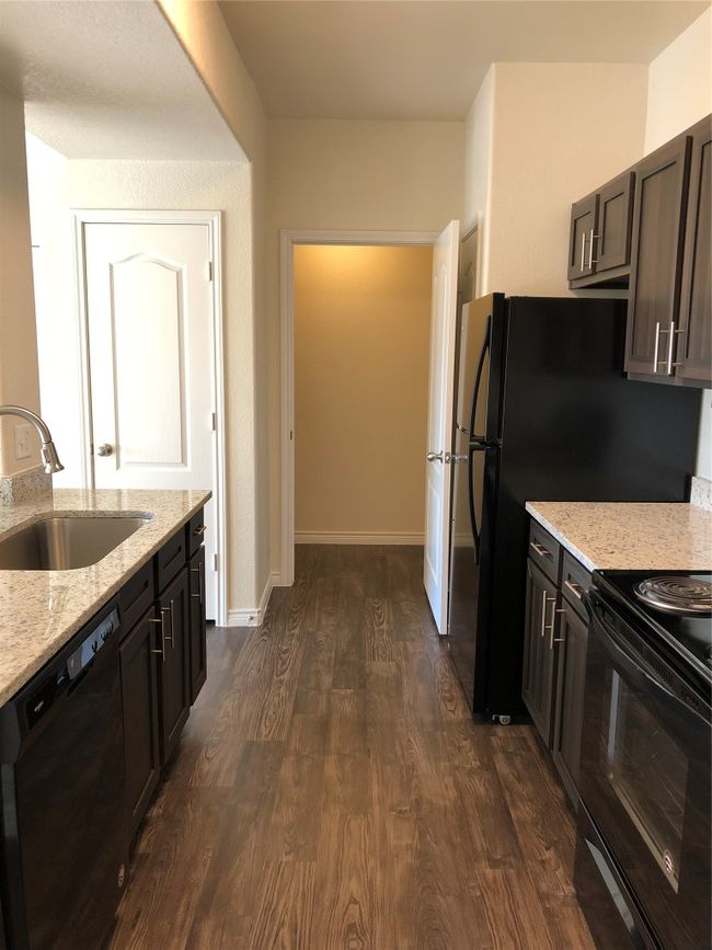 Kitchen featuring range, dark wood finished floors, light stone countertops, dishwasher, and a sink | Image 7
