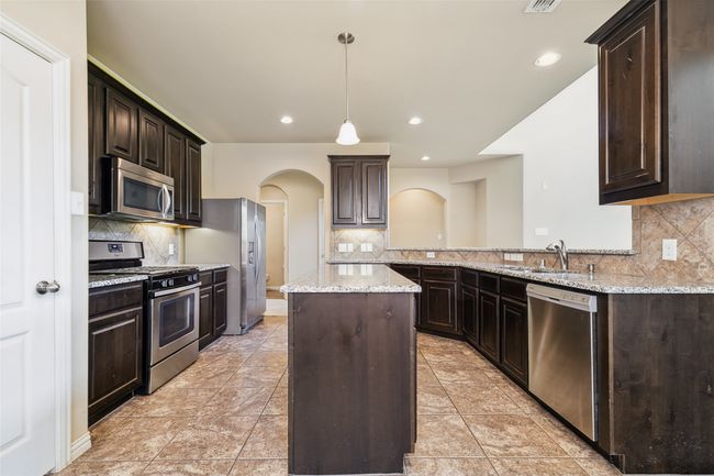 Kitchen featuring stainless steel appliances, a sink, arched walkways, a kitchen island, and decorative backsplash | Image 12