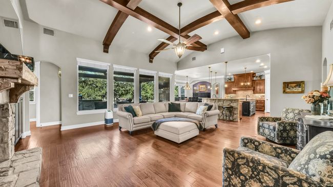Living area with high vaulted ceiling, a ceiling fan, a stone fireplace, beam ceiling, and dark wood-style floors | Image 12