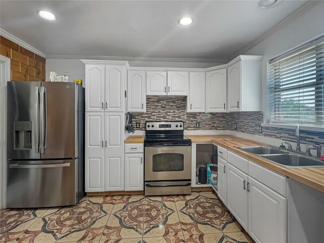 Kitchen featuring stainless steel appliances, ornamental molding, decorative backsplash, white cabinetry, and butcher block countertops | Image 17