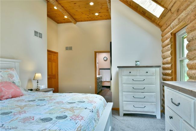Bedroom featuring wooden ceiling, high vaulted ceiling, a skylight, light carpet, and rustic walls | Image 27