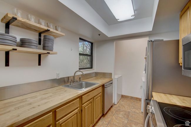 Kitchen featuring stainless steel appliances, sink, butcher block counters, and washer / dryer | Image 12