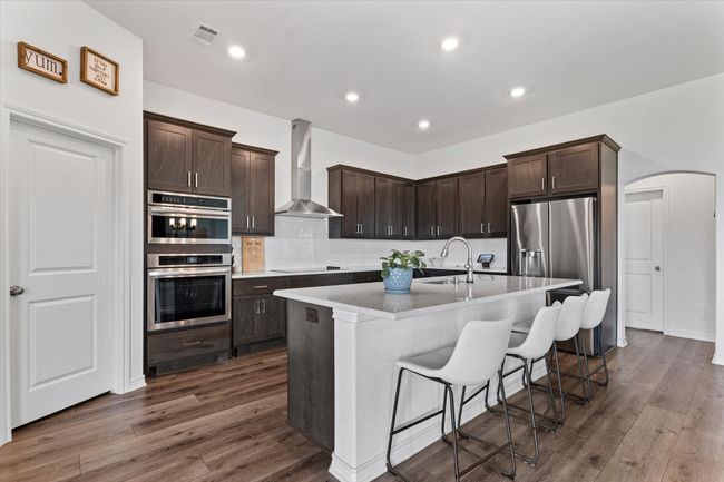 Kitchen featuring wall chimney range hood, visible vents, a sink, arched walkways, and dark brown cabinetry | Image 16