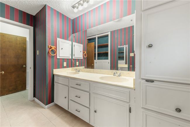 Full bathroom featuring wallpapered walls, double vanity, tile patterned floors, and a textured ceiling | Image 14