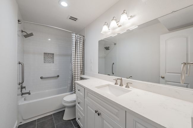 Bathroom with tile patterned floors, vanity, visible vents, toilet, and shower / bath combo with shower curtain | Image 13