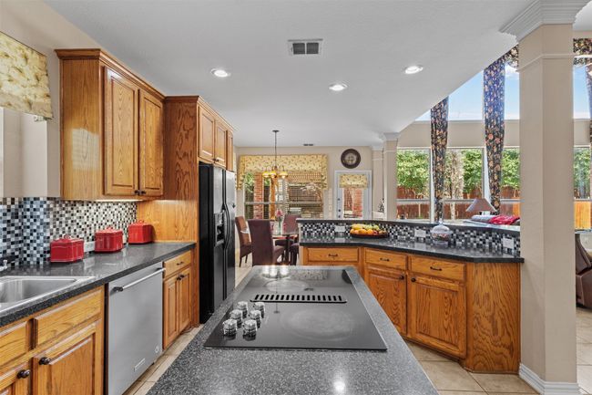 Kitchen featuring black appliances, dark countertops, tasteful backsplash, decorative columns, and a chandelier | Image 9