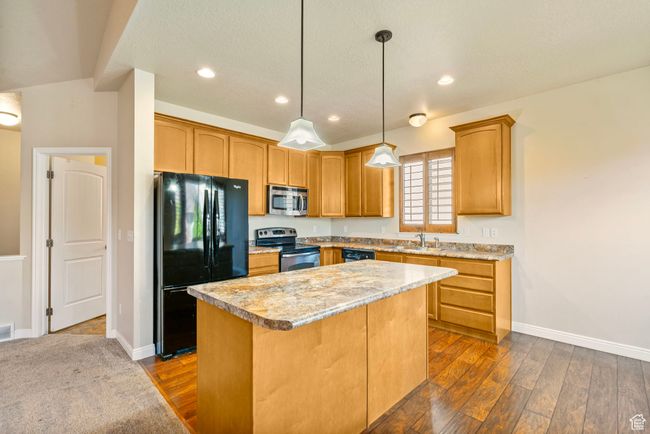 Kitchen featuring dark wood-style flooring, light countertops, a center island, and appliances with stainless steel finishes | Image 5