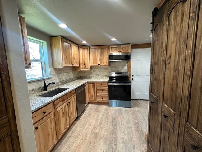 Kitchen featuring a sink, light wood finished floors, light stone countertops, stainless steel appliances, and decorative backsplash | Image 18