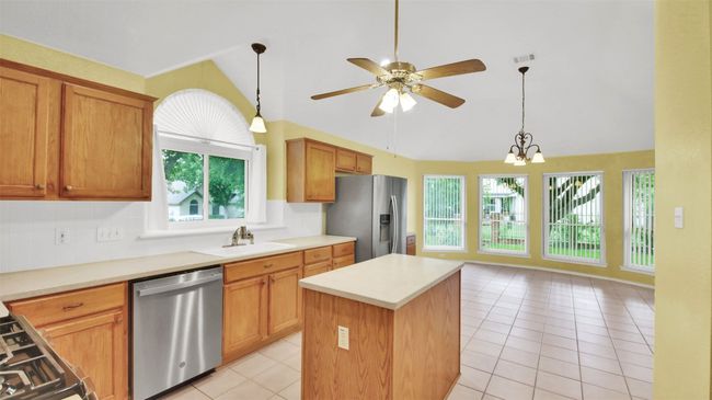 Kitchen with stainless steel appliances, vaulted ceiling, light tile patterned floors, a center island, and ceiling fan | Image 15