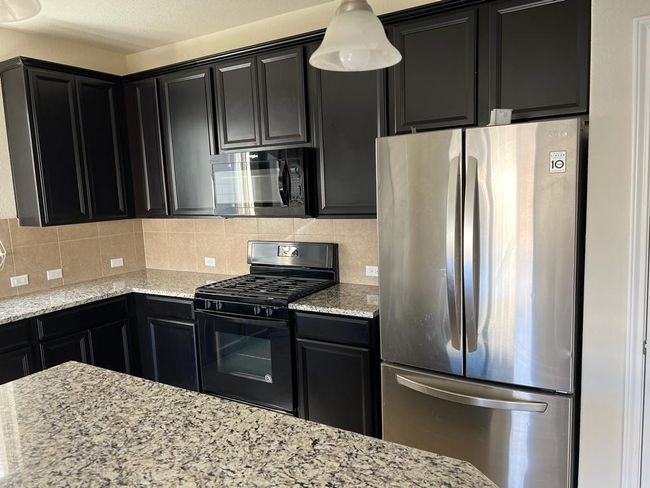 Kitchen with black appliances, dark cabinetry, light stone counters, and decorative backsplash | Image 10