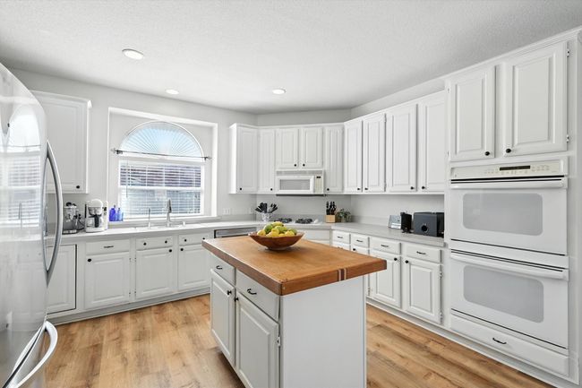 Kitchen with appliances with stainless steel finishes, wood counters, light wood-type flooring, white cabinets, and a kitchen island | Image 13