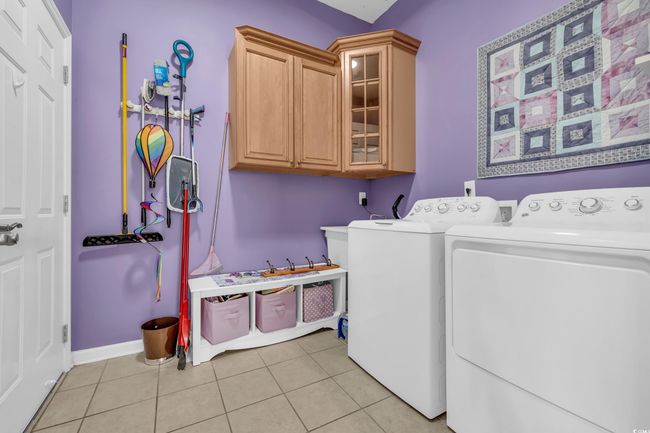 Washroom featuring light tile patterned floors, cabinet space, washing machine and dryer, and baseboards | Image 6